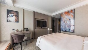 Una habitació d'hotel amb un llit, una taula amb una cadira, una televisió i obres d'art a les parets.