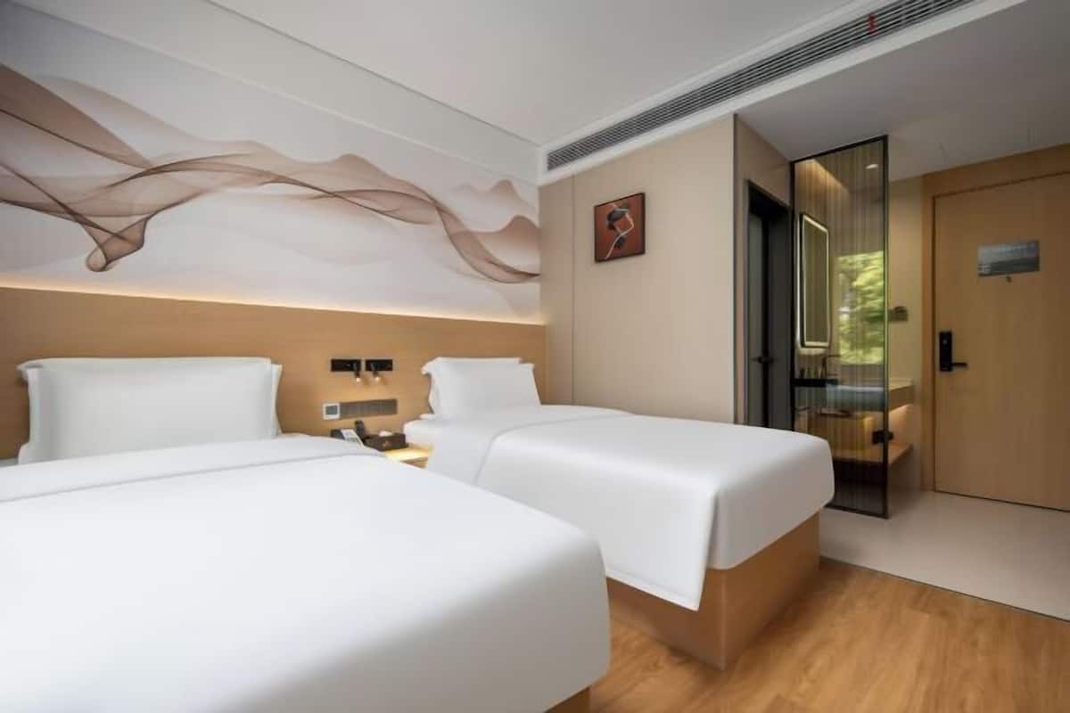 A hotel room with two beds, a modern ceiling design, a wooden door, and a small artwork on the wall.