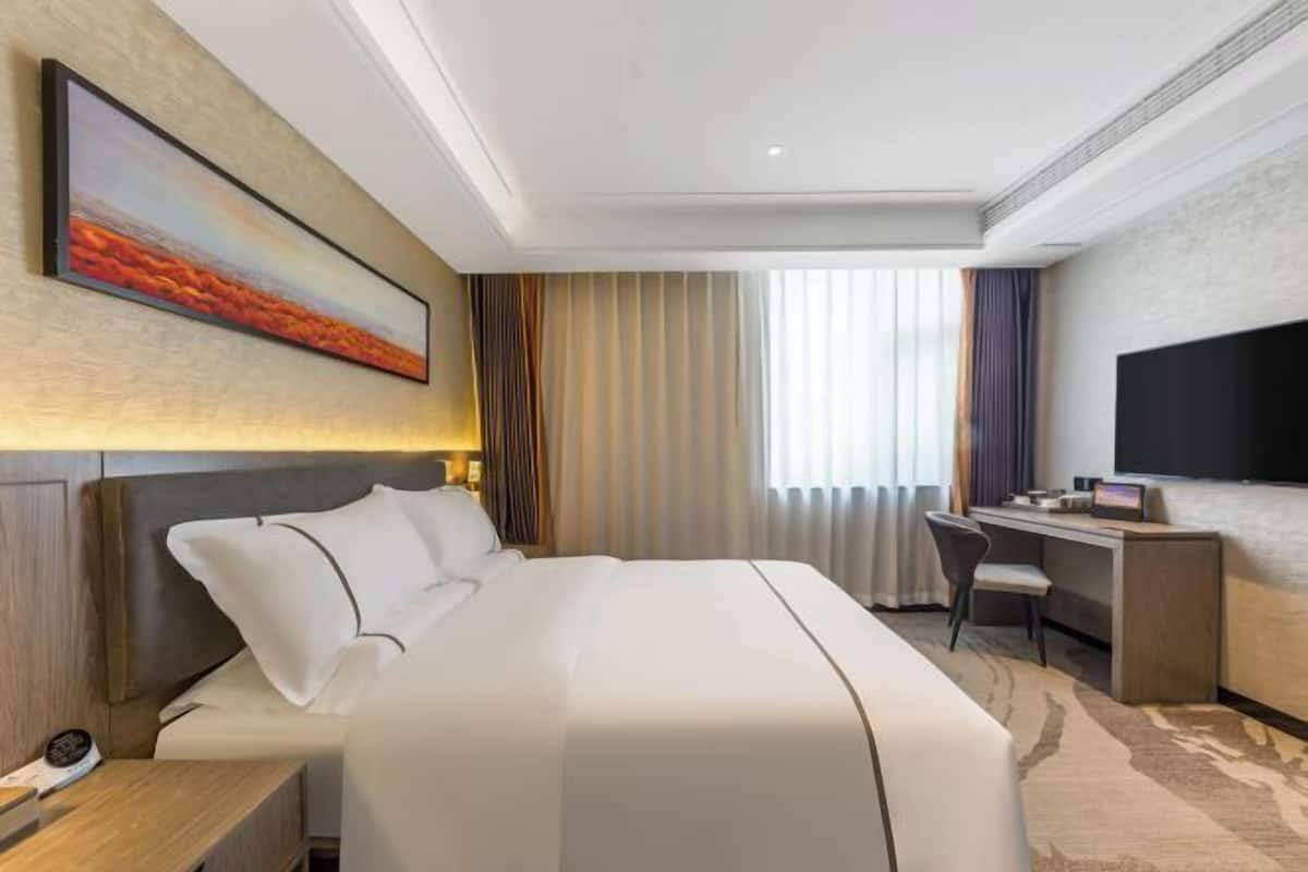 A modern hotel room with a large bed, a desk, a flat-screen TV, and a painting on the wall.