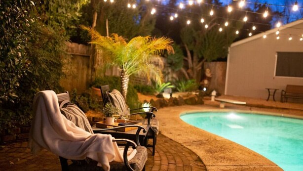 A poolside area with lounge chairs, a small table with a tray, and string lights. - The Paso House | Family Fun For All (Redding)