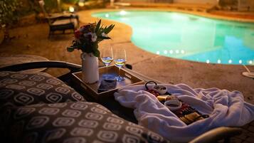 A poolside setting with a lounge chair, a tray with snacks and drinks, and a flower vase.
