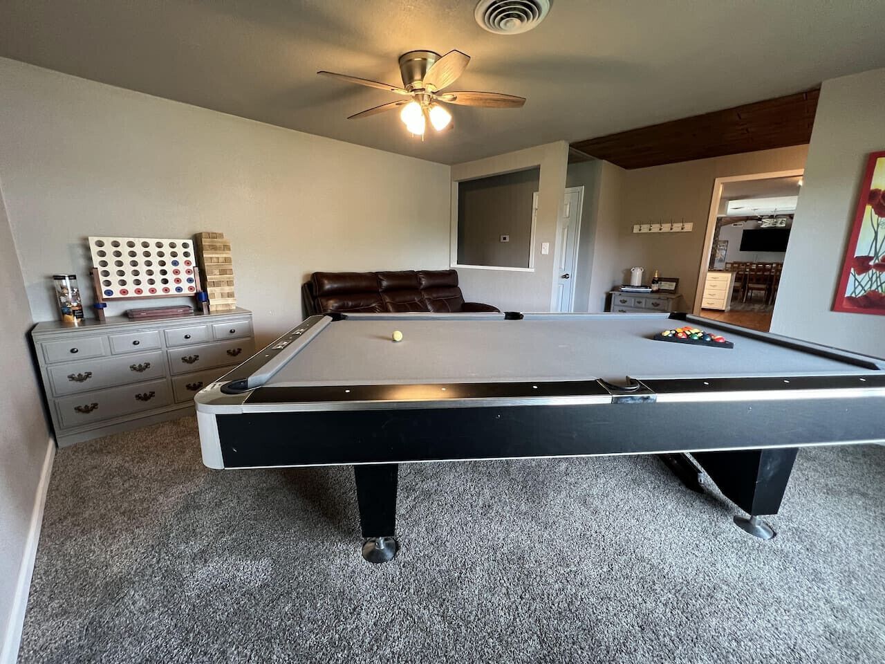 A pool table with a ceiling fan, a dresser, and a wall-mounted pinball machine.