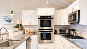 Una cocina moderna con armarios blancos, encimeras de granito, electrodomésticos de acero inoxidable y suelo de madera.