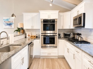 Une cuisine moderne avec des meubles blancs, des plans de travail en granit, des appareils électroménagers en acier inoxydable et un plancher en bois.
