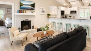Una sala de estar moderna con chimenea, un sofá, una mesa de centro y una zona de cocina con taburetes de bar.