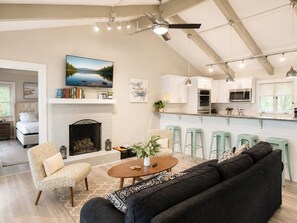 Un salon moderne avec une cheminée, un canapé, une table basse et un coin cuisine équipé de tabourets de bar.