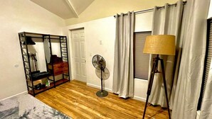 A bedroom with a wooden floor, a standing fan, a mirror, a bed, and a window with curtains. - Perfect, fully furnished 1-bed condo  (Black Canyon City)