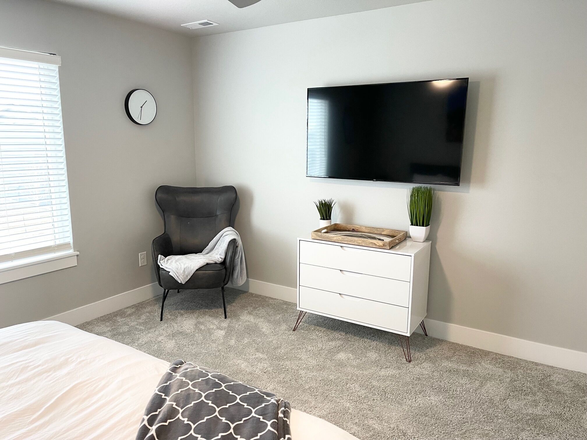 Une chambre à coucher avec un lit, une chaise, une commode, un téléviseur et une horloge au mur.