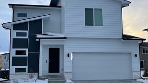 Une maison moderne à deux étages, dotée d’un garage, d’une porte d’entrée et d’une grande fenêtre.