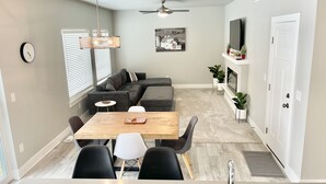 Un salon moderne avec une table à manger en bois, des canapés gris et une cheminée.