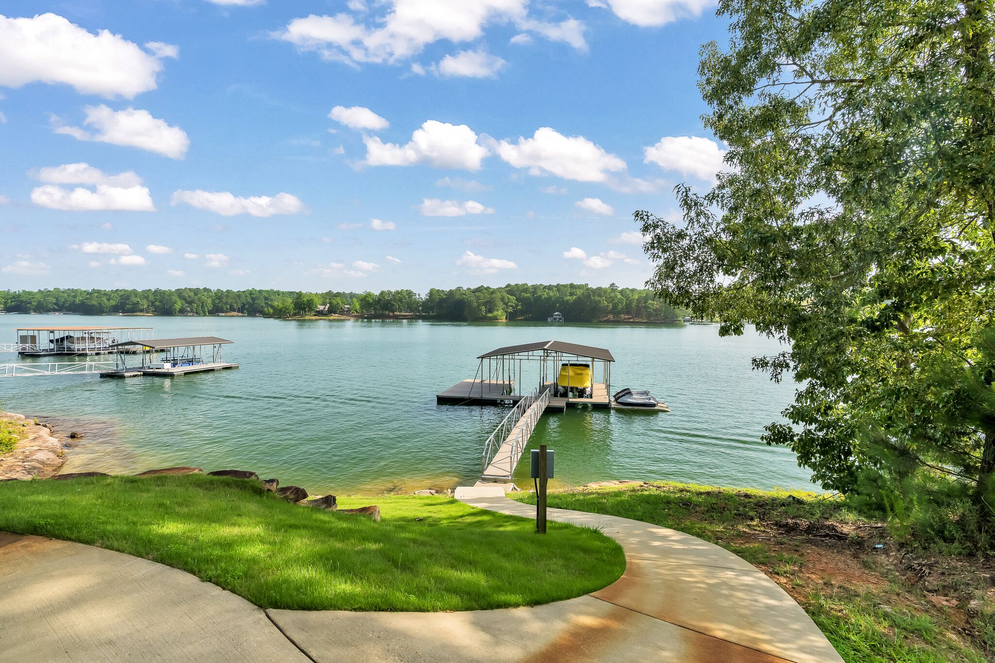 A lakeside view with a dock, a covered boat launch, and a grassy area.