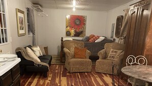 A cozy living room with a wooden parquet floor, a sofa set, a dining table with chairs, and a painting on the wall. - Country Cottage on the farm, peaceful, stars and fireflies! Sleeps 4! (Edmonton)