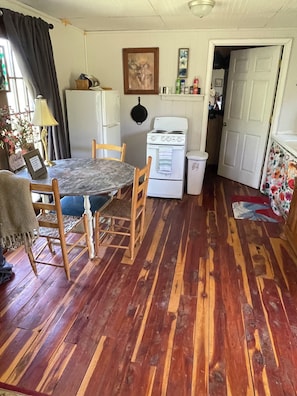 Una cocina con suelo de madera, una mesa de comedor, sillas, una estufa y un refrigerador.
