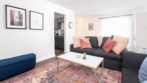 A living room with a sofa, a coffee table, and a rug. There are framed pictures on the wall. - City Condo with Outdoor Pool Near Broadway (Nashville)