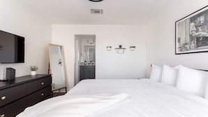 A bedroom with a large bed, a dresser, a TV, a mirror, and a door leading to a bathroom. - City Condo with Outdoor Pool Near Broadway (Nashville)