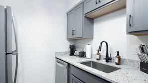 A modern kitchen with grey cabinets, a stainless steel refrigerator, a granite countertop, and a black faucet. - City Condo with Outdoor Pool Near Broadway (Nashville)