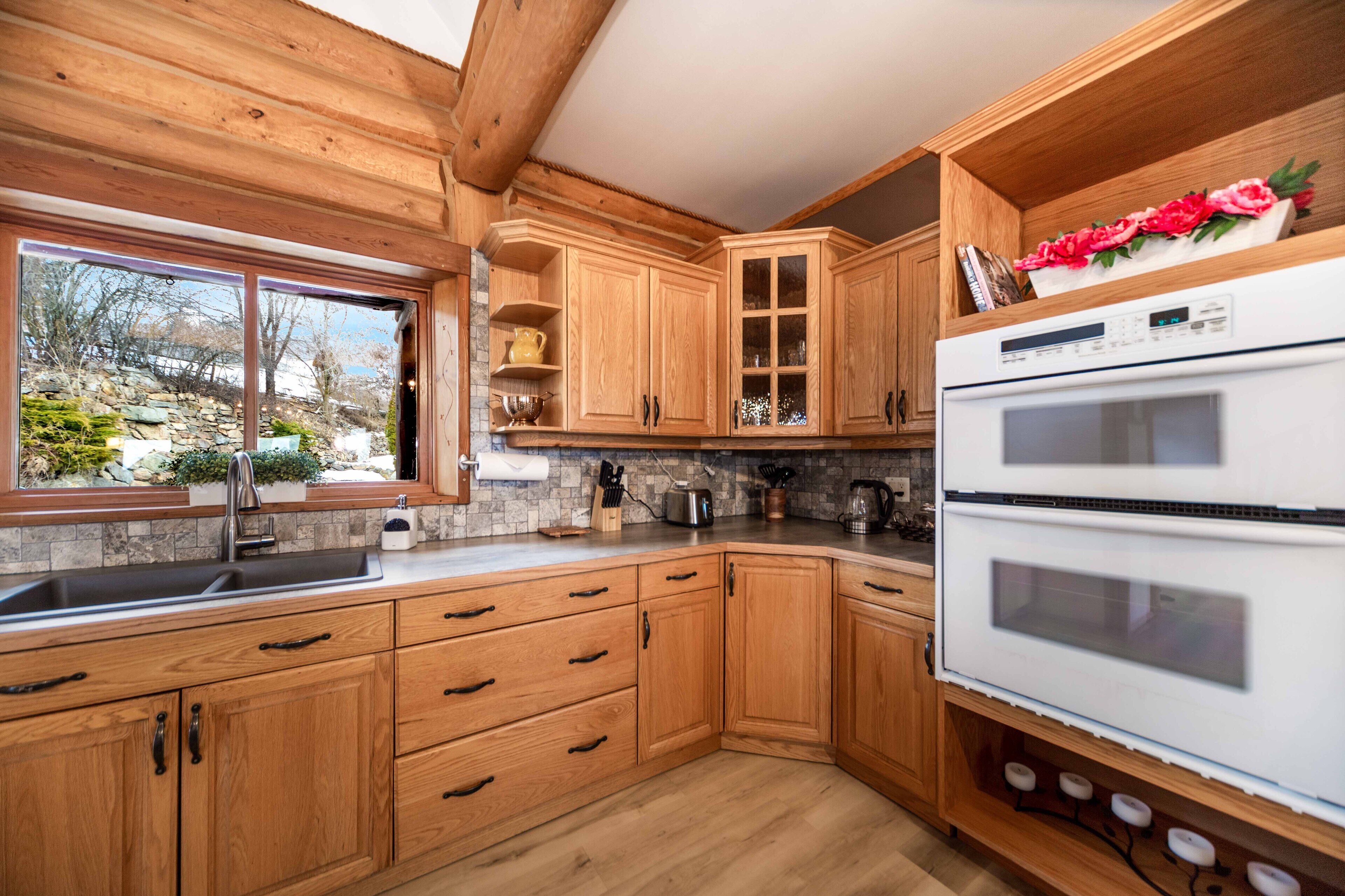 A kitchen with wooden cabinets, a double oven, and a window with a view of the outdoors.