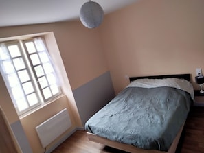 A bedroom with a bed, a window, a radiator, and a nightstand with a lamp. - MANTA House (Courtils)
