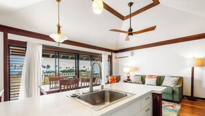 A kitchen with a large window, a ceiling fan, and a dining area with a table and chairs. - Kiahuna Plantation Ocean View with AC, REMODELED, 1 Bedroom, Sleeps 4 (Poipu)