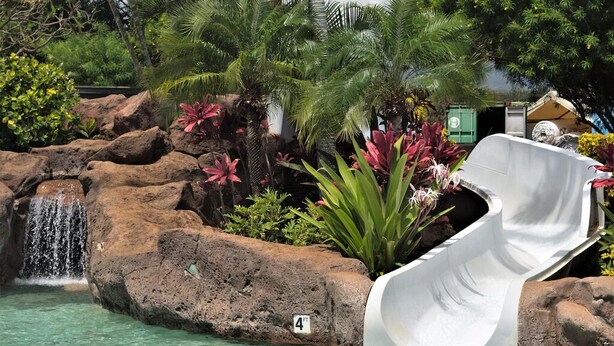 A water slide in a tropical setting with a rocky pool and lush greenery. - Kiahuna Plantation Ocean View with AC, REMODELED, 1 Bedroom, Sleeps 4 (Poipu)