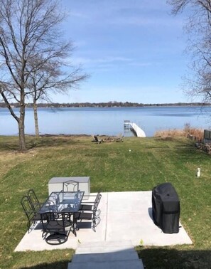 Een achtertuin met een patio tafel en stoelen, een barbecue en uitzicht op een meer.