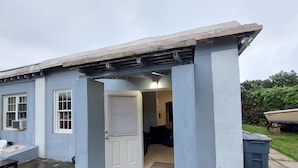 A small, single-story building with a concrete exterior, a covered porch, and a door leading to an interior space. - 1-bed House Sleeps 2 With Parking (Sandys Parish)