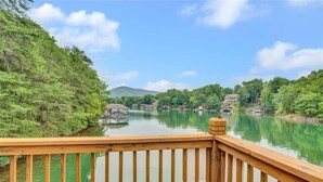 Une terrasse en bois surplombe une rivière paisible, avec des bâtiments situés sur la rive opposée.
