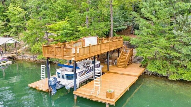 Une terrasse en bois avec un bateau amarré en dessous, le tout entouré d’une végétation luxuriante.