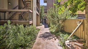 A narrow concrete pathway flanked by dense greenery and wooden fences, leading to a building with multiple balconies and a visible staircase. - Private Riverside Ski Retreat  2/2 condo close to Beaver Creek and Vail (Avon)