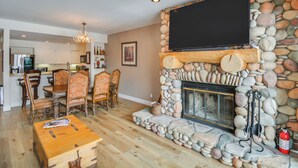 A living room with a stone fireplace, a television mounted above it, and a dining area with wooden furniture. - Private Riverside Ski Retreat  2/2 condo close to Beaver Creek and Vail (Avon)