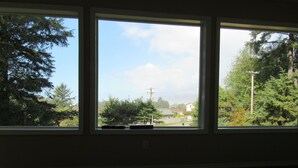 A room with three windows, each with a view of a residential area, trees, and a clear sky. - Peregrine's Nest (Smith River)