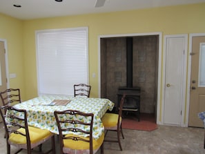 Un coin repas avec une table dressée pour quatre personnes, des chaises avec des coussins jaunes, une cheminée et une porte donnant sur une autre pièce.