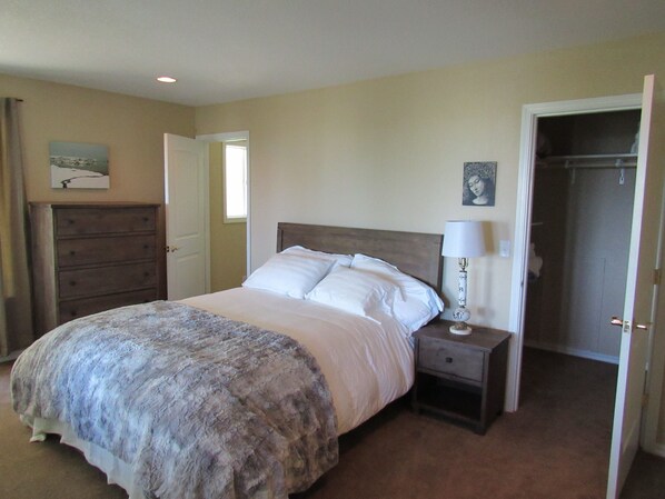 Une chambre à coucher comprenant un lit, une table de chevet, une commode et une porte donnant sur un placard.