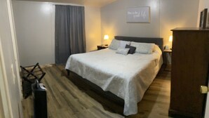 Habitación de hotel con una cama grande, dos mesitas de noche con lámparas, piso de madera y una cortina en la ventana.