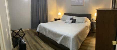 A hotel room with a large bed, two bedside tables with lamps, a wooden floor, and a curtain on the window.
