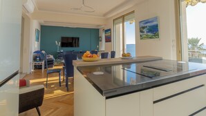 A modern kitchen with a central island, a dining area with blue chairs, and a large window offering a view of the sea. - 3-Br Apartment, Sea View, by the Beaches (Cannes)
