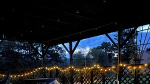 Una terraza de madera con alfombra estampada, mobiliario exterior e iluminación con luces colgantes.