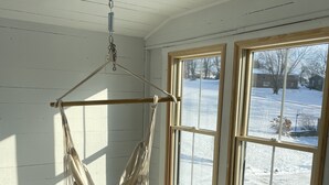 Una habitación con una hamaca colgante, ventanas amplias y una colchoneta morada para ejercicio.