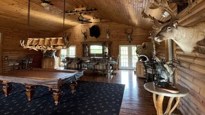 A spacious log cabin interior with a dining area, a fireplace, and antler decorations.