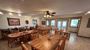 A spacious dining area with wooden tables and chairs, a ceiling fan, and large windows allowing natural light.