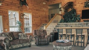 A log cabin interior with a living room, a fireplace, a staircase, and a dining area.