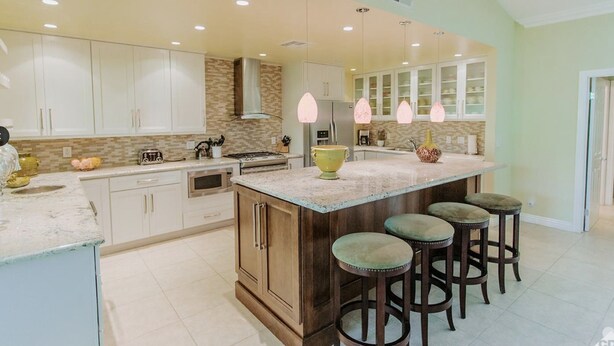 A kitchen with white cabinets, a large island with stools, and pendant lighting. - Classic Avondale  Private  Country Club ~ Gated community front gate security (Palm Desert)