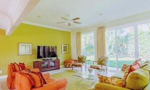 A living room with a television, sofa, chairs, and a large window with curtains. - Classic Avondale  Private  Country Club ~ Gated community front gate security (Palm Desert)