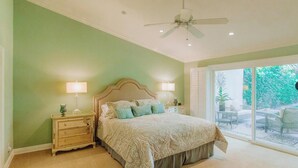 A bedroom with a large bed, two bedside tables with lamps, a ceiling fan, and a sliding glass door leading to an outdoor patio. - Classic Avondale  Private  Country Club ~ Gated community front gate security (Palm Desert)