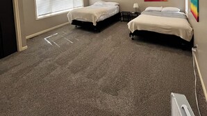 Une chambre avec deux lits, un ventilateur de plafond, une fenêtre avec des stores et un tableau abstrait coloré accroché au mur.