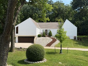 Uma casa de dois andares com garagem, varanda frontal e gramado bem cuidado.