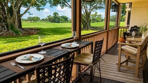 Un espace extérieur abrité, aménagé pour les repas, avec vue sur un terrain de golf, du mobilier en bois et une lanterne.