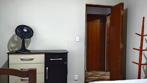 Una habitación con una cama, un escritorio con un ventilador, un armario y una silla de madera.