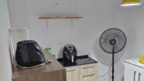 Una cocina pequeña con cafetera, ventilador y hervidor sobre la encimera.