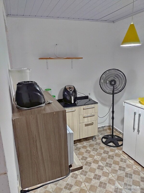 Une petite cuisine équipée d’une machine à café, d’un ventilateur et d’une bouilloire posés sur le plan de travail.